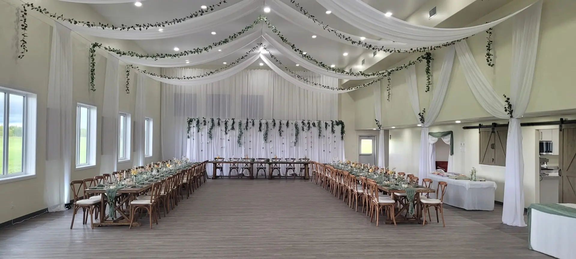 The hall at Bristol Event Centre set with long tables, white linens and a draped ceiling for a wedding reception